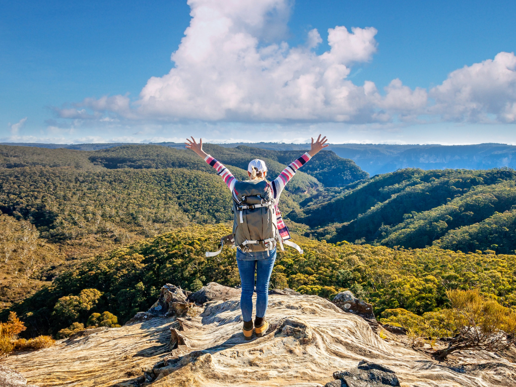 A lady is standing on a mountain with her hands in the air